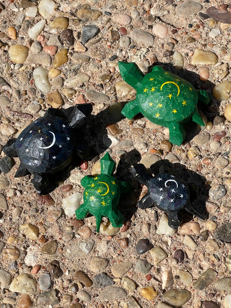 K&ouml;nnte beinhalten: Vier h&ouml;lzerne Schildkr&ouml;tenfiguren mit bemalten Designs. Zwei Schildkr&ouml;ten sind gr&uuml;n mit gelben Sternen und einem Halbmond. Zwei Schildkr&ouml;ten sind schwarz mit wei&szlig;en Sternen und einem Halbmond.