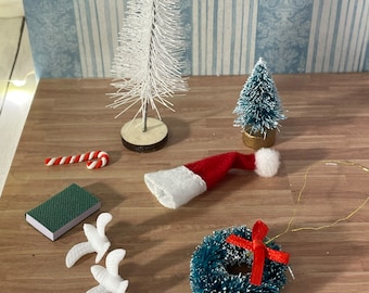 May include: A collection of miniature Christmas decorations including a white and a green artificial Christmas tree, a red Santa hat, a green book, a candy cane, two white doves, and a green wreath with a red bow.