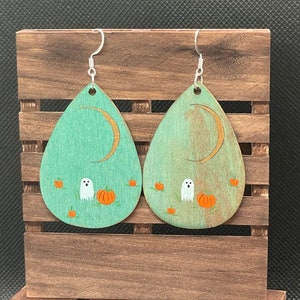 May include: Teal wooden teardrop shaped earrings with a crescent moon, ghost, and pumpkins painted on them.