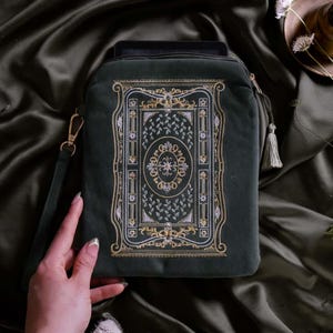 Könnte beinhalten: Dunkelgrüne Tablet-Hülle aus Samt mit einem gestickten Design. Das Design zeigt ein zentrales Medaillon und florale Motive in Gold- und Weißgarn. Inklusive Handschlaufe und Quaste.