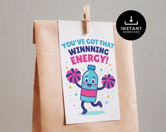 May include: A brown paper gift bag with a white tag attached by a wooden clip. The tag features a cartoon bottle character with pom-poms and the text "YOU'VE GOT THAT WINNING ENERGY!" A black circle with a download icon is in the upper right.