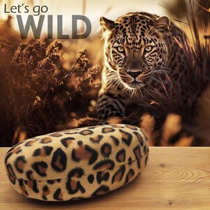 May include: A leopard print glasses case with a fuzzy texture. The case is on a wooden surface with a blurred image of a leopard in the background. The text "Let's go WILD" is in the top left corner of the image.