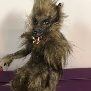 May include: A handmade werewolf doll with brown fur, a snarling expression, and green eyes. The doll is standing on a wooden base.