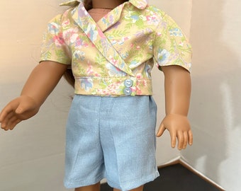 Puede incluir: Una muñeca con un par de pantalones cortos de color azul claro y una blusa de estampado floral amarillo con cuello blanco. La muñeca lleva zapatos blancos.