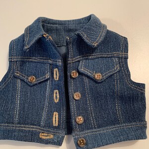 May include: A blue denim vest with a collared neckline and multiple button closures. The vest has two front pockets and a single button on the bottom.