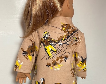 Puede incluir: Una camisa de muñeca marrón con un estampado de un hombre pescando y un faisán. La camisa tiene mangas largas y cuello alto.