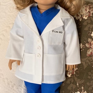 Puede incluir: Bata blanca de m&eacute;dico con un top de quir&oacute;fano azul debajo. La bata tiene un bolsillo en el lado izquierdo con una etiqueta de nombre que dice "D Lee MD".