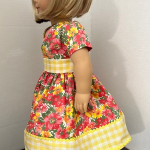 May include: A red and yellow floral dress with a yellow and white gingham belt and trim. The dress is made for a doll.