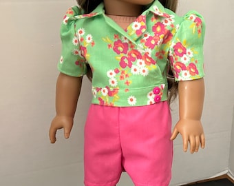 Puede incluir: Una muñeca con una camisa de estampado floral verde y rosa y pantalones cortos rosas con zapatillas blancas.