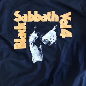 May include: Black Sabbath Vol. 4 t-shirt with a gold print on a dark blue background. The image features a black and white silhouette of a person with wings.