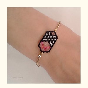 May include: A gold chain bracelet with a black and white beaded charm featuring a pink and white heart design.