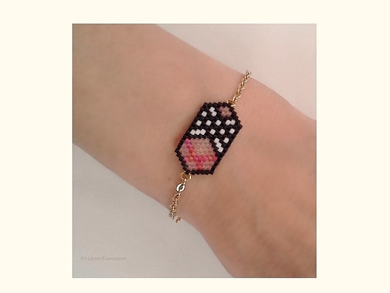 May include: A gold chain bracelet with a black and white beaded charm featuring a pink and white heart design.