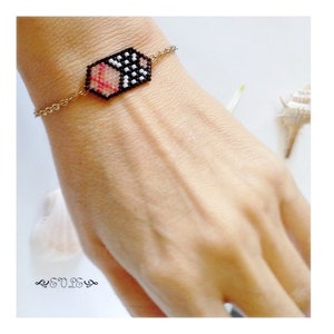 May include: A gold chain bracelet with a black, white, and pink beaded hexagon charm.