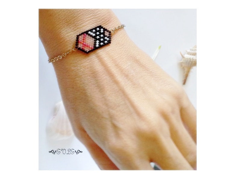 May include: A gold chain bracelet with a black, white, and pink beaded hexagon charm.