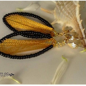 May include: A pair of gold earrings with black beads and yellow thread. The earrings are shaped like a teardrop and have a delicate, feminine design.