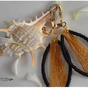 May include: A pair of gold earrings with black and gold beads. The earrings are oval shaped and have a fringe of gold thread.