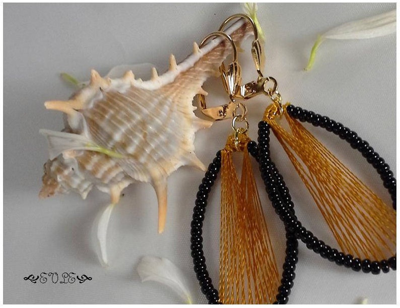 May include: A pair of gold earrings with black and gold beads. The earrings are oval shaped and have a fringe of gold thread.