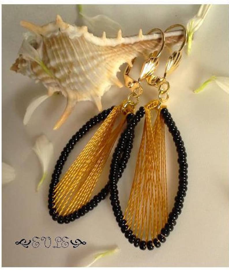 May include: A pair of gold and black earrings with a fringe design. The earrings are made with black beads and gold thread.