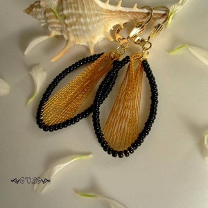 May include: A pair of gold and black dangle earrings with a woven design. The earrings are oval shaped and have a clip-on closure.