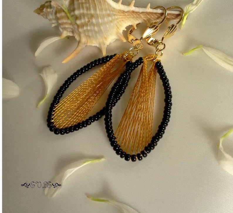 May include: A pair of gold and black dangle earrings with a woven design. The earrings are oval shaped and have a clip-on closure.