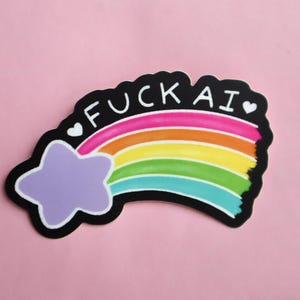 A sticker of a purple shooting star with a rainbow tail that has the works "F-ck AI" above it with two hearts on either side of the text.