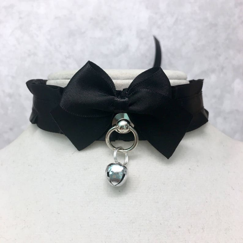 May include: A black satin choker with a large bow and a silver bell charm.