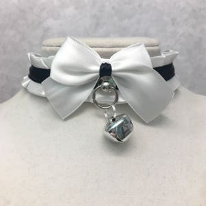 May include: White satin choker with a black ribbon and a silver bell charm.