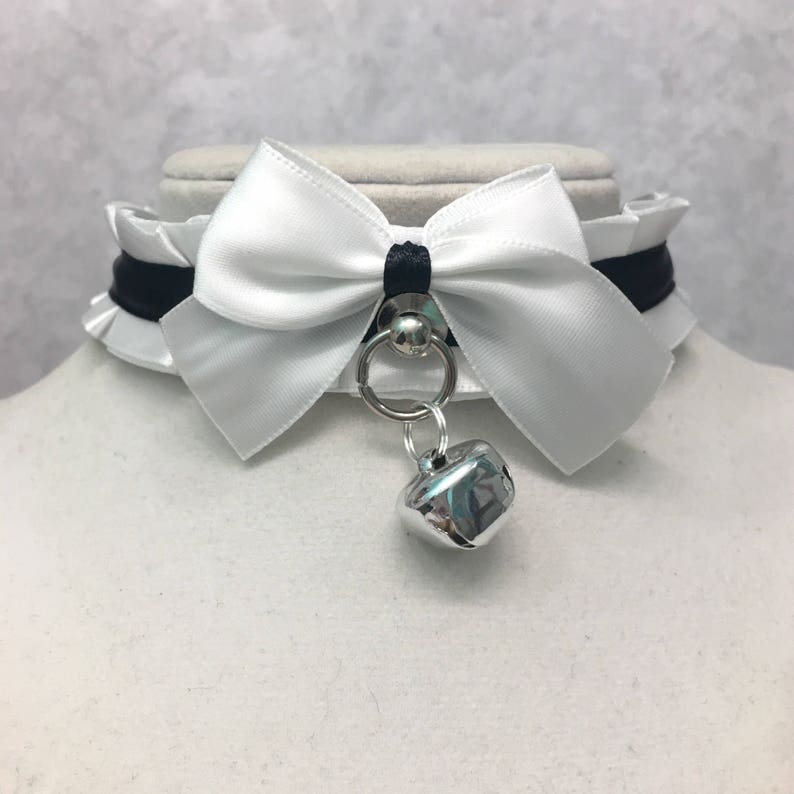 May include: White satin choker with a black ribbon and a silver bell charm.