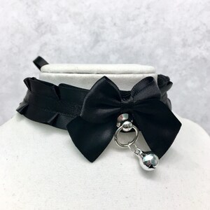 May include: Black satin choker with a large black satin bow and a silver bell charm.