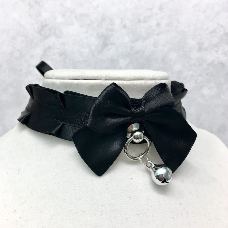 May include: Black satin choker with a large black satin bow and a silver bell charm.