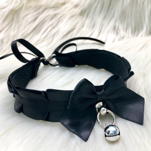 May include: Black satin choker with a large bow and a silver bell charm.