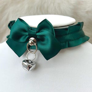 May include: A green satin choker with a large bow and a silver bell charm.