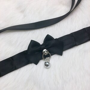 May include: Black satin choker with a large black satin bow and a silver bell charm.