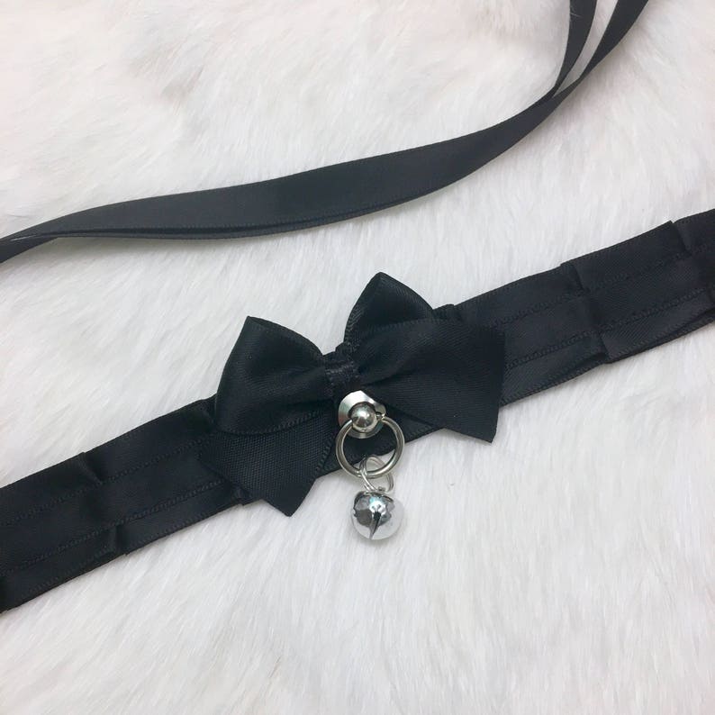 May include: Black satin choker with a large black satin bow and a silver bell charm.