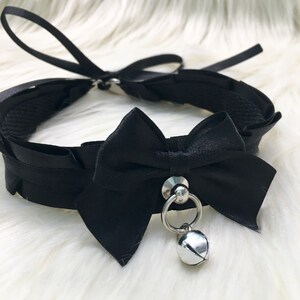 May include: Black satin choker with a large black bow and a silver bell charm.