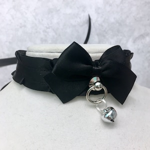 May include: A black satin choker with a large black satin bow and a silver bell charm.