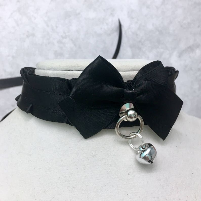 May include: A black satin choker with a large black satin bow and a silver bell charm.