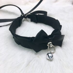 May include: Black choker necklace with a large black satin bow and a silver bell charm.