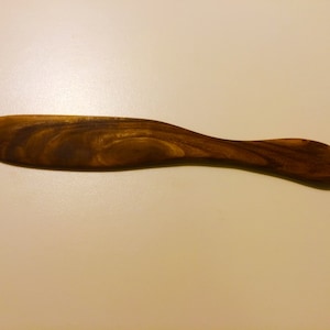 May include: A wooden butter knife with a dark brown finish and a smooth, rounded handle.