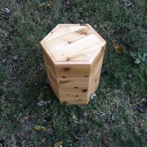 Puede incluir: Un taburete hexagonal de madera con un acabado de madera natural. El taburete est&aacute; hecho de madera de cedro y tiene un dise&ntilde;o simple y r&uacute;stico.
