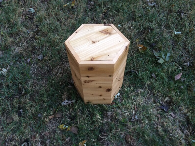 Puede incluir: Un taburete hexagonal de madera con un acabado de madera natural. El taburete est&aacute; hecho de madera de cedro y tiene un dise&ntilde;o simple y r&uacute;stico.