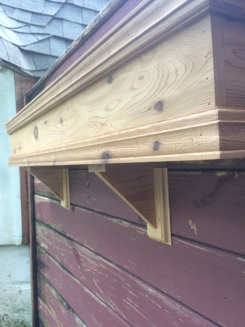 Puede incluir: Un estante de madera con un borde decorativo, montado en una pared de madera roja. El estante est&aacute; soportado por dos soportes triangulares de madera.