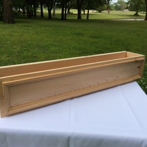 May include: A natural wood planter box with a simple design. The planter is made of unfinished wood and has a rectangular shape.