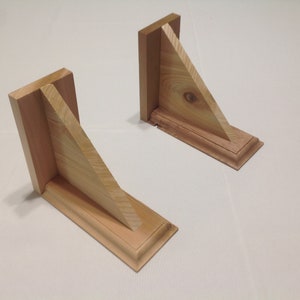 May include: Two wooden shelf brackets with a triangular shape and a decorative trim. The brackets are made of light wood and have a natural finish.