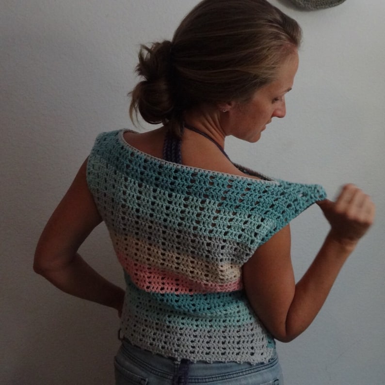 Puede incluir: Un top de crochet sin mangas con un patr&oacute;n a rayas en tonos de azul, rosa y beige. El top tiene un escote amplio y redondo y un ajuste holgado.