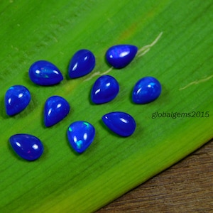 May include: Ten teardrop-shaped blue opals with iridescent flashes of color. The opals are arranged on a green leaf.
