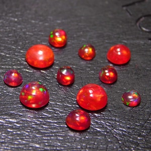 May include: A collection of ten red opal cabochons of varying sizes, with iridescent flashes of color.
