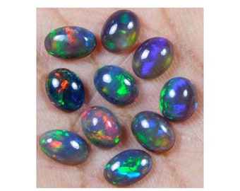 May include: A collection of oval-shaped black opals with iridescent green, blue, and red flashes. The opals are arranged on a light brown surface.