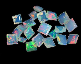 May include: A collection of iridescent white opal gemstones, cut into square shapes. The opals have a rainbow sheen and are scattered on a black background.