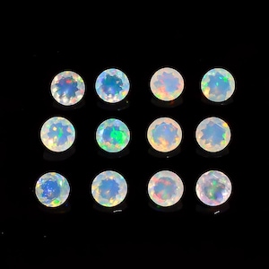 May include: Twelve round, faceted opals are arranged against a black background. The opals display a range of colors, including blue, green, and orange, with a shimmering, iridescent effect. The gemstones are of similar size and shape.